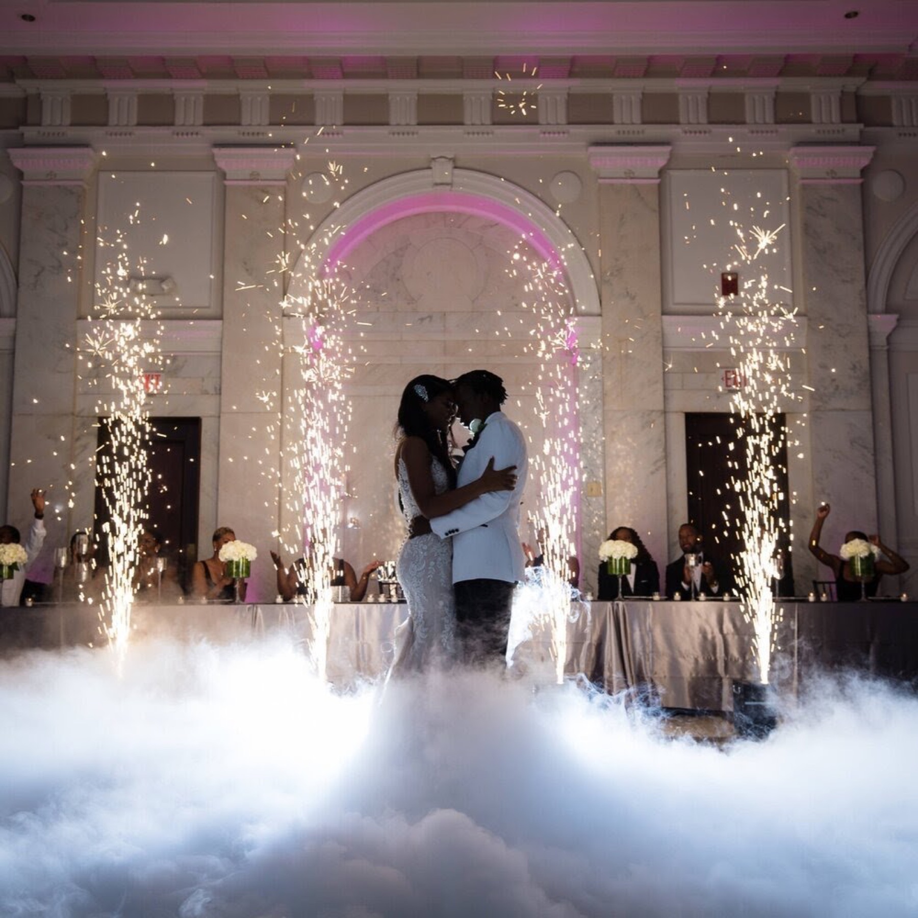 Bride and groom kissing between cold spark fountains and low fog