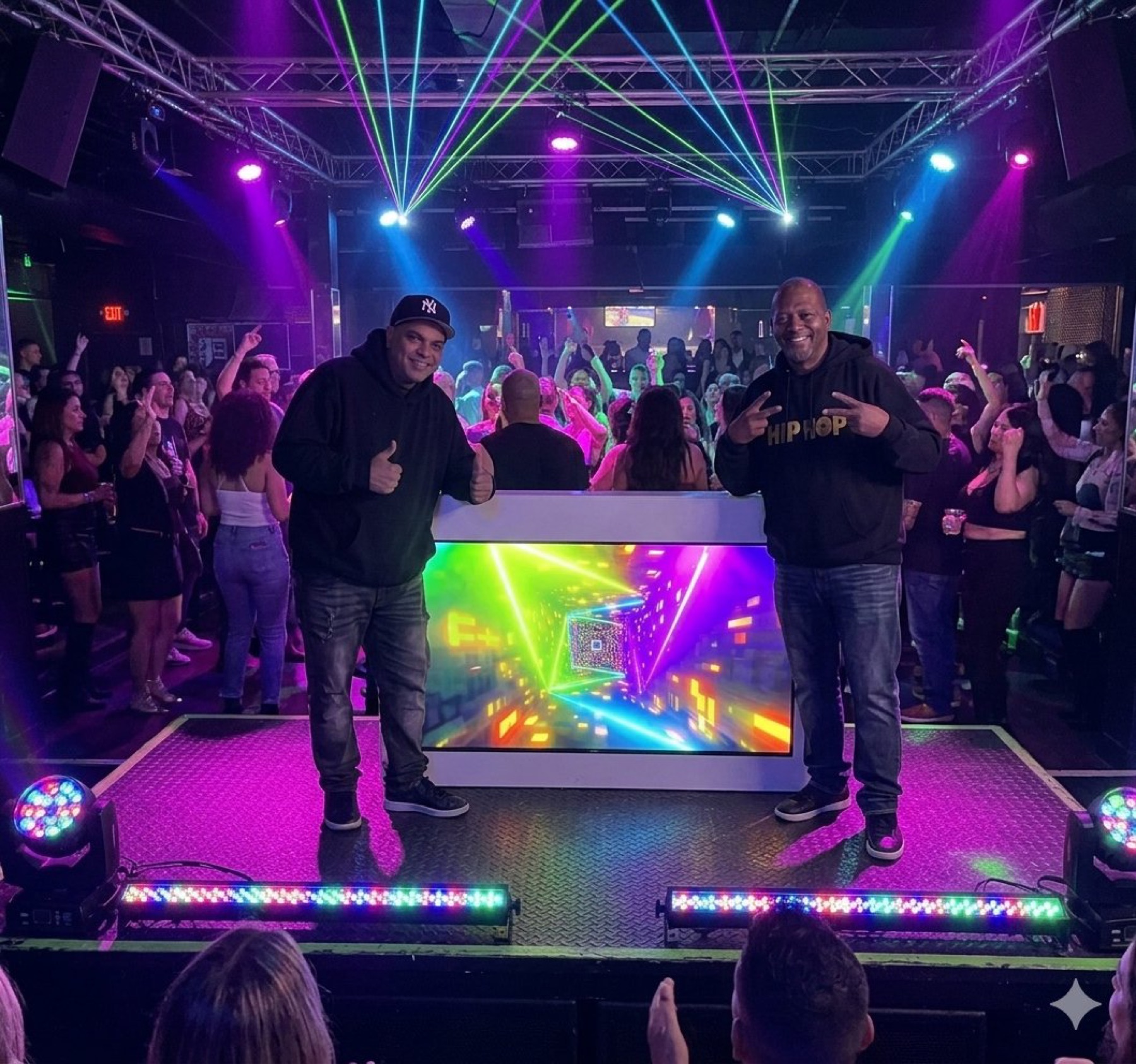 Two DJs posing at an LED DJ booth under laser lights with a crowd behind