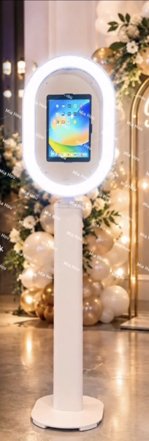 Selfie photo booth stand with a ring light beside a balloon arch