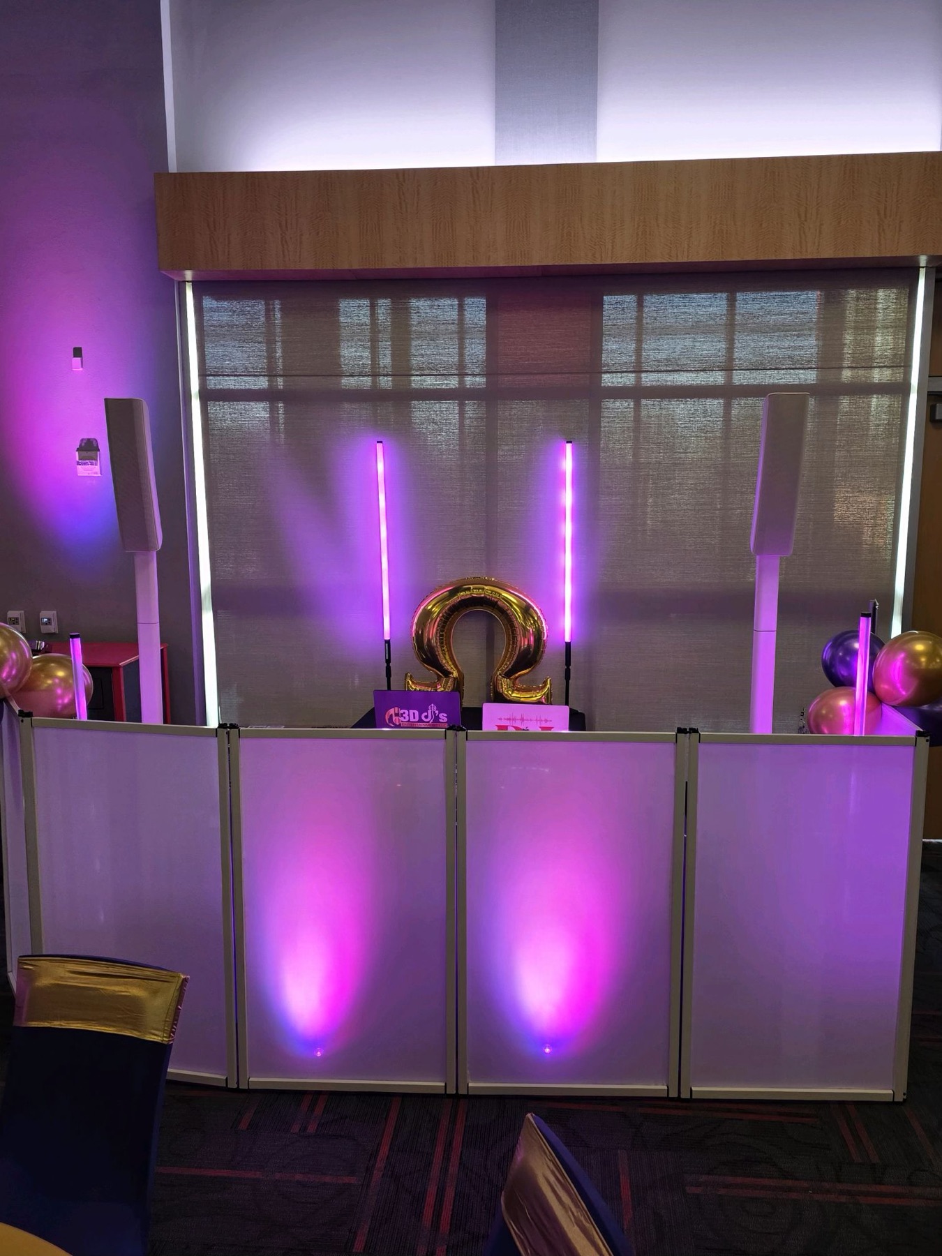 White DJ facade with purple uplighting, light tubes and a gold Omega balloon