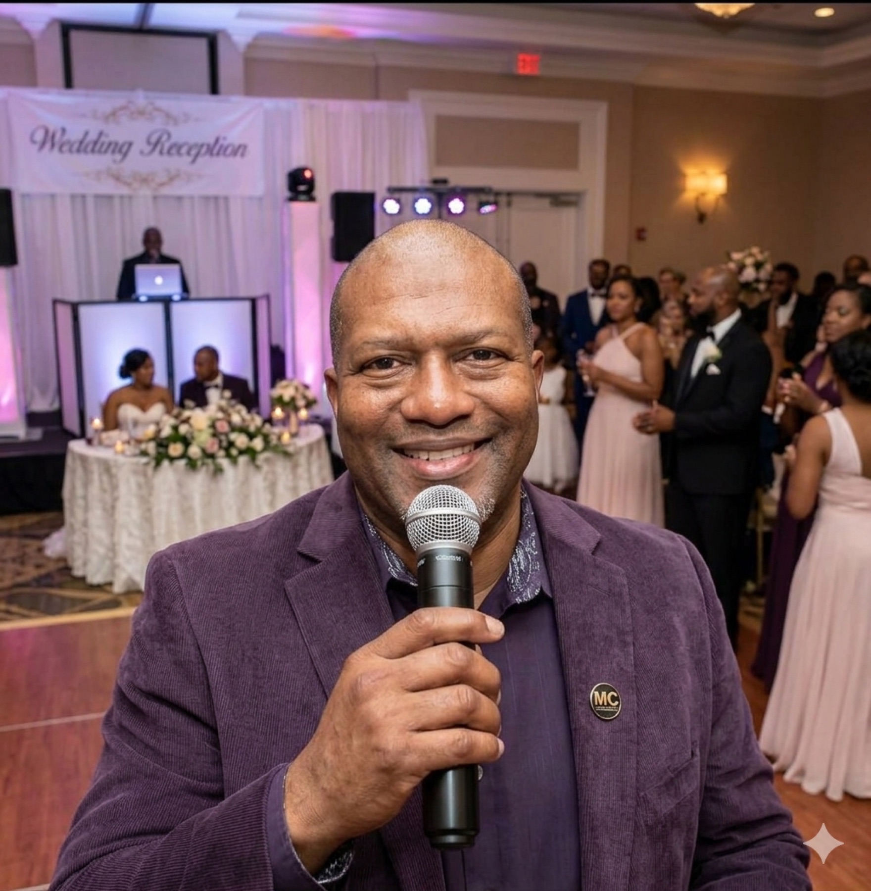 MC holding a microphone at a wedding reception with the couple at the head table