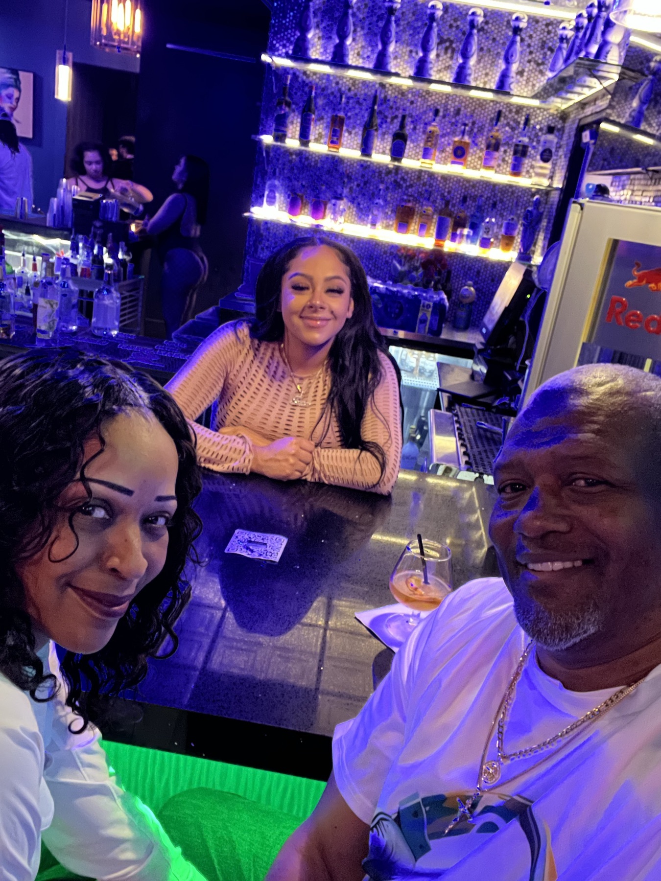Selfie with two guests at a bar with backlit bottle shelves