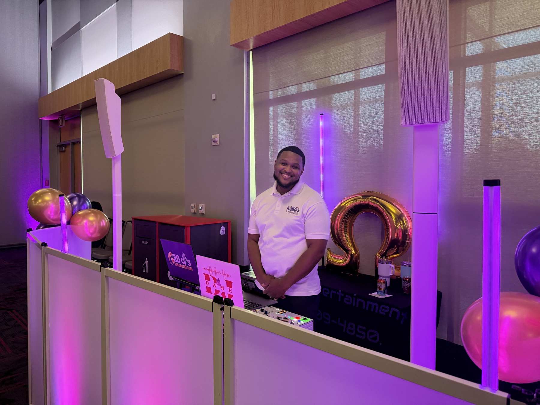 DJ in a 3D DJ's polo behind a white facade with purple light tubes and balloons
