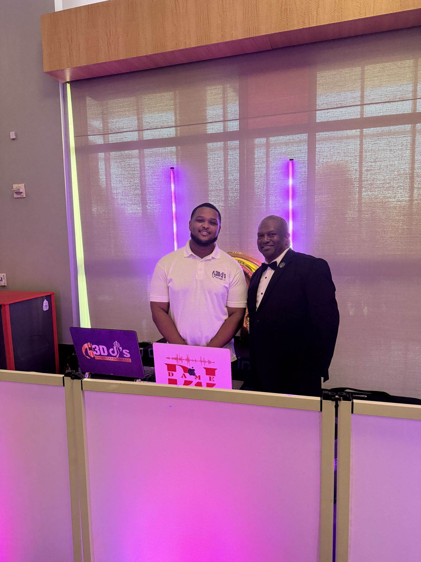 DJ and a man in a tuxedo standing behind the DJ facade