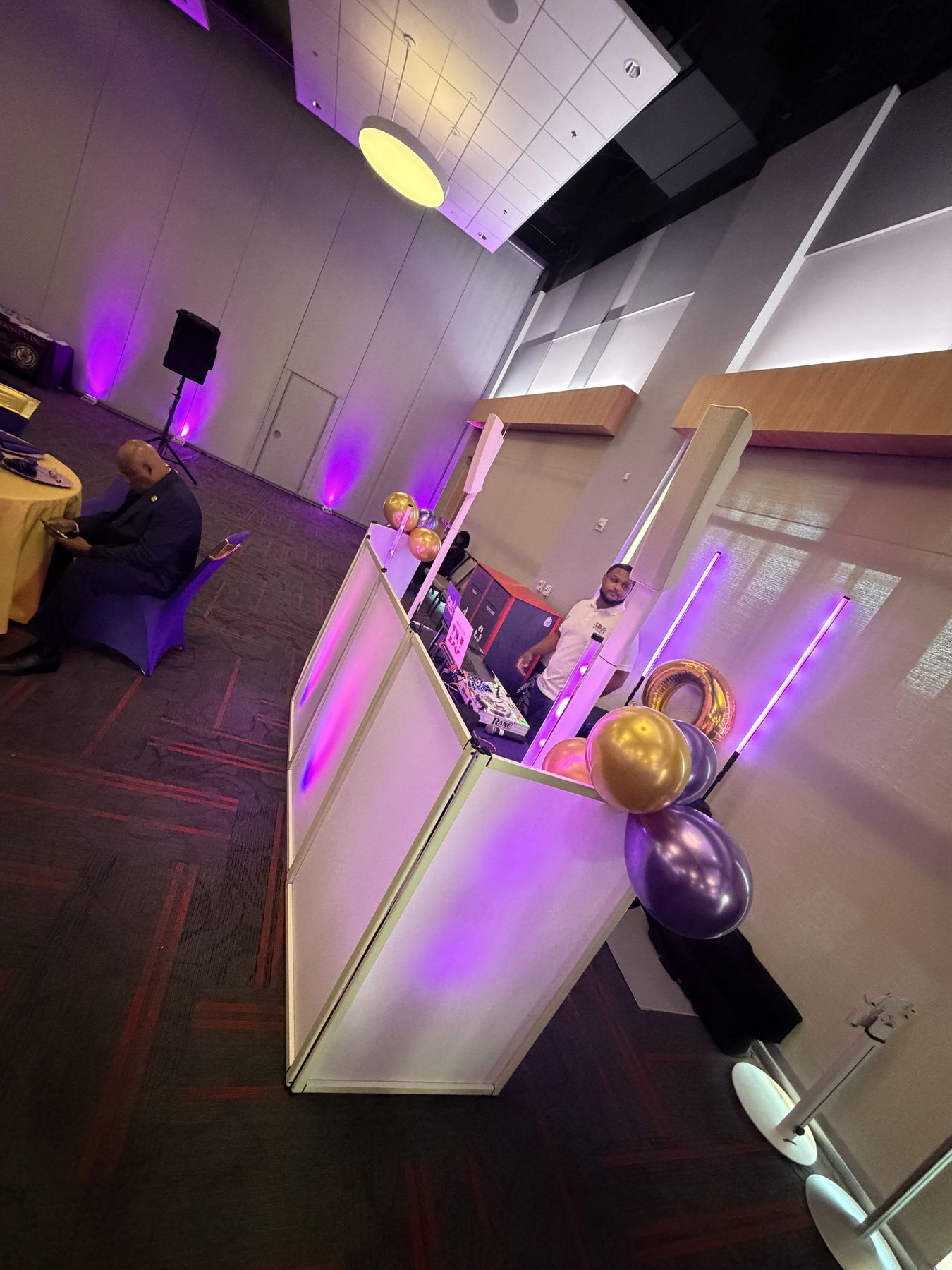 White DJ facade with purple balloons and light tubes in an event hall